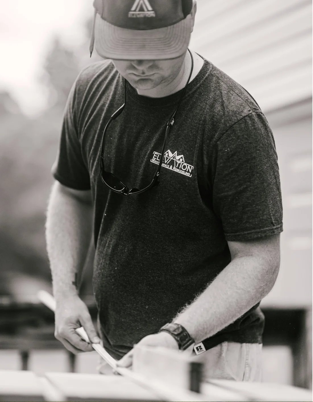 Man in dark t-shirt and cap looking down while working with hands on table, black and white photo