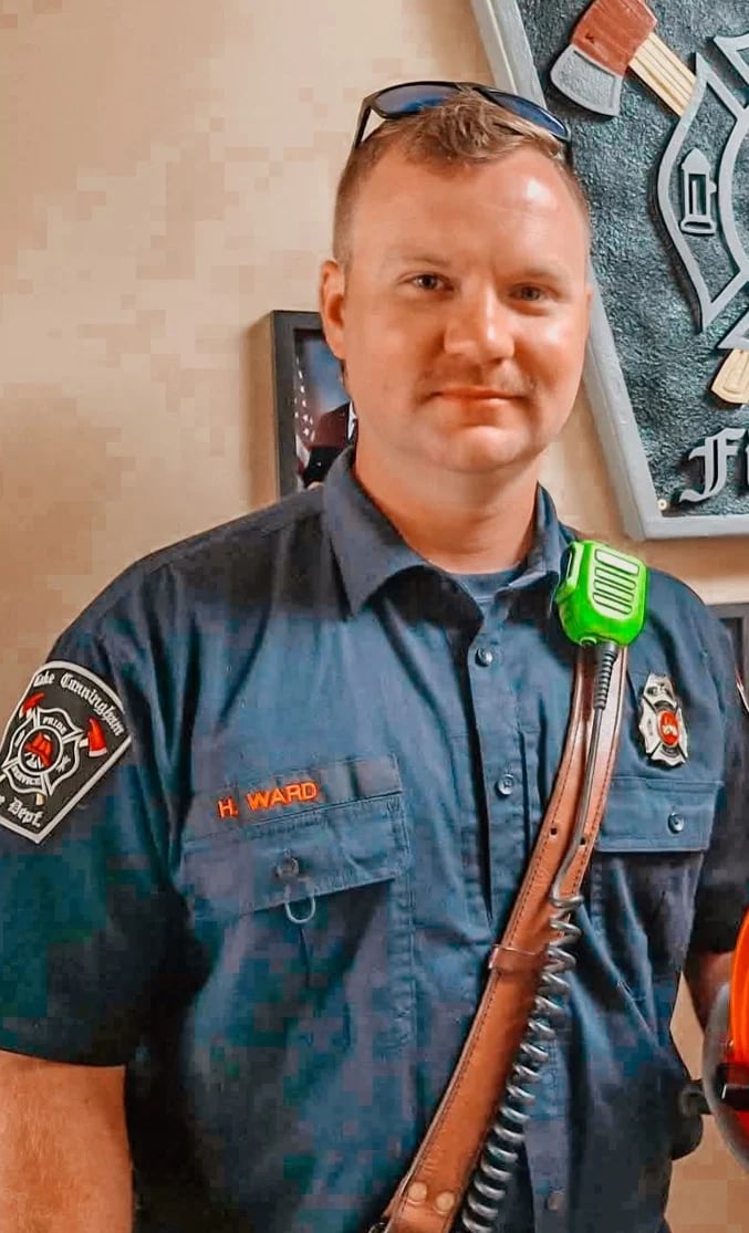 Male firefighter in dark blue uniform with name tag H. Ward, wearing sunglasses on head and radio on shoulder strap